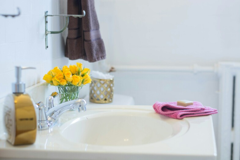 WC:n allas, jonka ympärillä pinkki siivousrätti, käsisaippuapumppu ja keltaisia kukkia