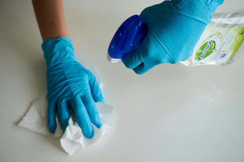 Kädet, joissa siniset siivoushanskat putsaavat tasoa talouspaperilla ja pesuaineella. 