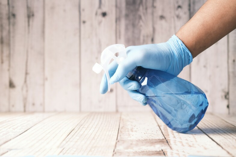 Sininen siivousainepullo kädessä, jossa sininen siivoushanska.