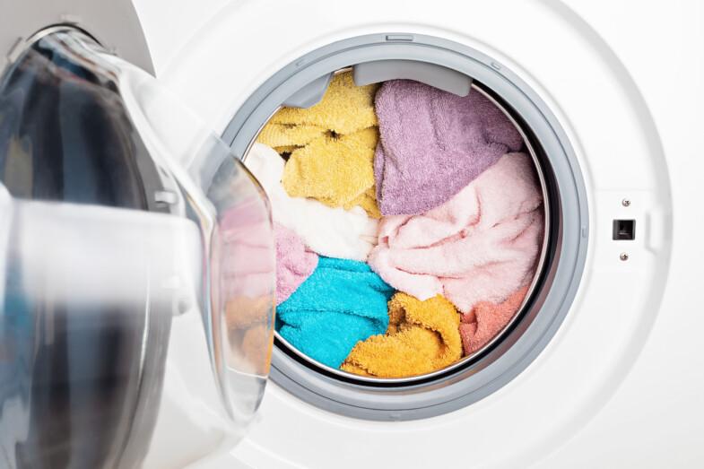 Täysi pyykinpesukone auki, jossa eri värisiä pyykkejä. 