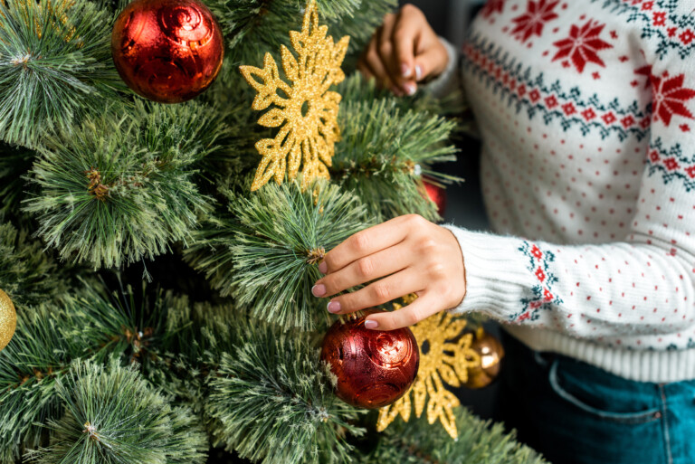 Lähikuva naisesta koristelemassa joulukuusta kultaisilla ja punaisilla koristeilla.