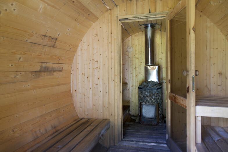 Rustiikkinen pyöreäpuinen sauna, jossa puukiuas ja yksinkertaiset puupenkit.