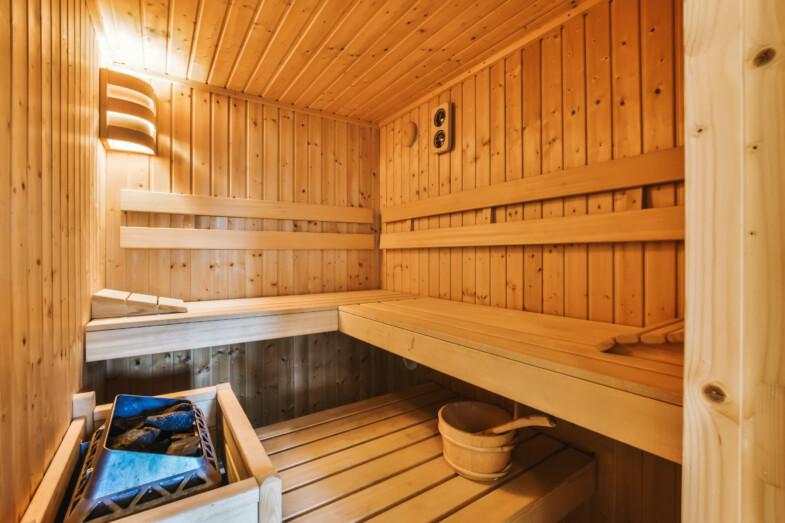 Perinteinen suomalainen sauna, jossa puiset lauteet, sähkökiuas ja kiulu alalauteella.